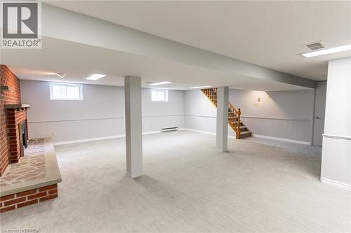 Spacious finished basement featuring light-toned carpeting, a brick fireplace with a stone hearth, recessed lighting, and paneling along the walls - 30 Proctor Avenue, Brantford, ON 