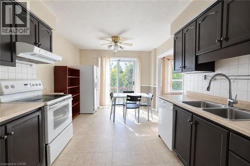 Kitchen featuring dark wood cabinetry, light-toned countertops, white tile backsplash, and a dual basin stainless steel sink with a pull-down faucet - 95 Resurrection Drive, Kitchener, ON 