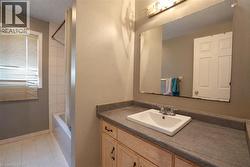 Bathroom featuring a single vanity with an integrated sink, a built-in mirror, and a tub with a shower enclosure - 