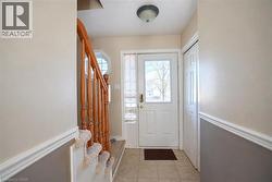 Tiled flooring entry with a white paneled door, natural wood staircase, and an octagonal window - 