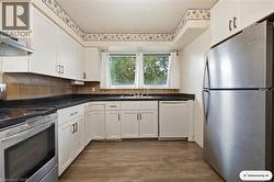 White cabinetry with dark hardware, dark countertops, brown tile backsplash, stainless steel appliances, and wood-finish flooring - 
