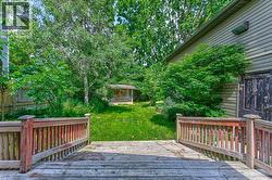 Expansive backyard featuring a wood deck with railings, lush green lawn, mature trees, and a wooden fence - 