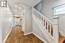 Entryway featuring a tiled floor, white baseboards, and a staircase with wood-finish treads and a white railing - 