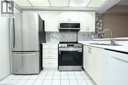 White cabinetry, stainless steel appliances, mosaic tile backsplash, white countertops, and white tile flooring - 