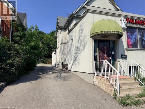 Building exterior featuring a light-colored stucco finish, a green fabric awning, and a prominent entrance with concrete steps and white railings - 612 King Street E, Kitchener, ON 