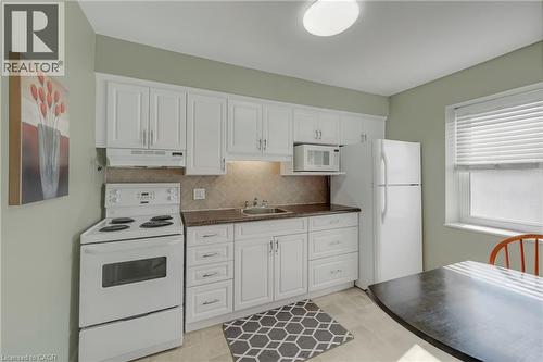 Kitchen featuring white cabinetry, dark countertops, a tile backsplash, and a window with blinds - 824 Brant Street Unit# 9, Burlington, ON 