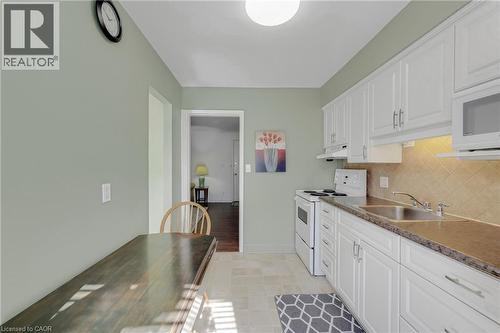 White cabinetry, tile backsplash, built-in microwave, under-cabinet lighting, and light-toned flooring - 824 Brant Street Unit# 9, Burlington, ON 