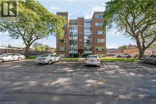Brick exterior building with multiple windows, surrounded by mature trees, and an asphalt parking lot - 824 Brant Street Unit# 9, Burlington, ON 