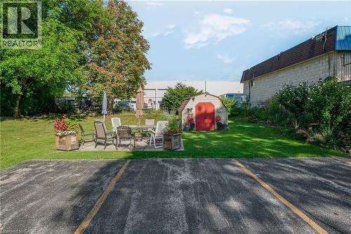 Expansive lawn with mature trees, a concrete patio, and a utility shed featuring red double doors - 824 Brant Street Unit# 9, Burlington, ON 
