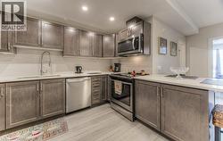 Kitchen featuring wood-finish cabinetry, stainless steel appliances, white subway tile backsplash, and light-toned countertops - 