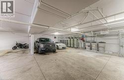 Concrete flooring in a subterranean parking area featuring exposed overhead utilities and column supports - 