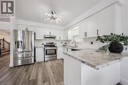 Contemporary kitchen featuring white cabinetry, stainless steel appliances, wood-finish flooring, a tile backsplash, and stone countertops - 