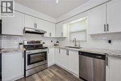 White shaker cabinetry, stainless steel appliances, subway tile backsplash, stone countertops, and wood-finish flooring - 