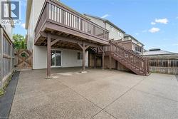 Spacious concrete patio with an elevated wooden deck featuring a full staircase, privacy fencing, and a sliding glass door - 