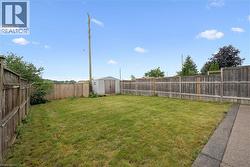Expansive backyard featuring a manicured lawn, full perimeter fencing, a concrete patio, and a utility shed - 