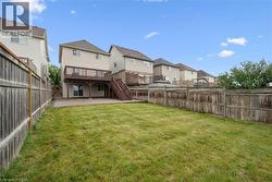 Expansive backyard featuring a manicured lawn, a large upper deck with wood railings, a lower patio, and privacy fencing - 