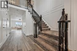 Foyer with wood-finish flooring, white paneled walls, and a carpeted staircase with dark wood balusters - 