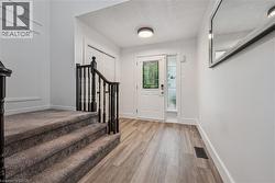 Entryway featuring wood-finish flooring, a white paneled door with decorative glass, and a carpeted staircase with dark wood balusters - 
