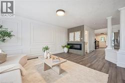Wood-finish flooring throughout, featuring a linear electric fireplace with fluted panel surround, decorative wall molding, and architectural columns - 