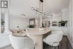 Open concept living space with wood-finish flooring, a linear bubble chandelier, built-in fireplace, paneled accent wall, and white cabinetry - 