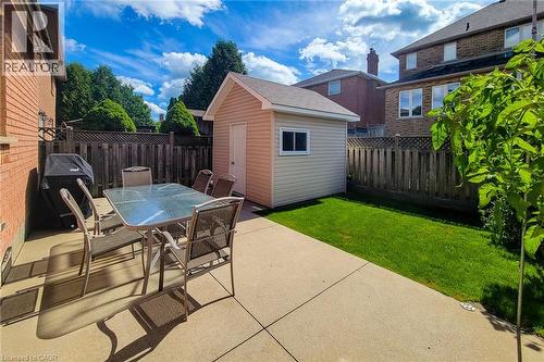 Concrete patio area, manicured lawn, wood fencing, and a detached storage shed with a window - 276 Greencedar Drive, Hamilton, ON 