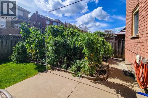 Private backyard with concrete patio, garden bed with mature plants, and wood privacy fencing - 276 Greencedar Drive, Hamilton, ON 