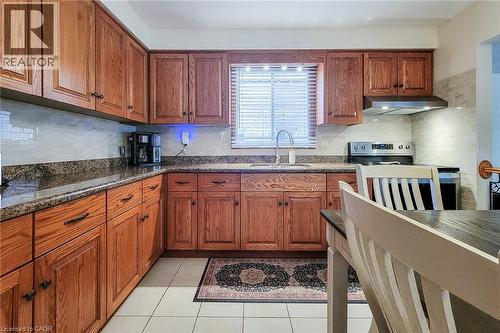 Kitchen featuring wood cabinetry, solid surface countertops, tile backsplash, stainless steel appliances, and tile flooring - 276 Greencedar Drive, Hamilton, ON 