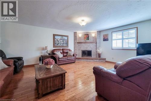 Wood-finish flooring throughout, a white brick fireplace with a wood mantle, white plantation shutters, and recessed ceiling lighting - 276 Greencedar Drive, Hamilton, ON 