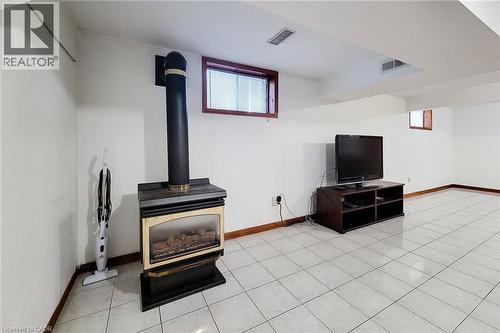 Freestanding fireplace with a black flue, white tile flooring, and wood-trimmed windows - 276 Greencedar Drive, Hamilton, ON 