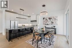 Open-concept kitchen and dining area featuring a large center island with dark countertop, stainless steel refrigerator, white cabinetry, wood-finish flooring, and a sliding glass door - 
