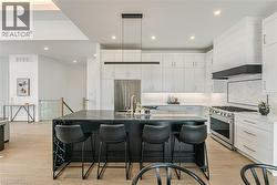 Contemporary kitchen featuring a large island with built-in wine storage, stainless steel appliances, light wood-finish flooring, and a glass-paneled staircase - 