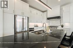 Gourmet kitchen with sleek black countertops, stainless steel appliances, white cabinetry, a built-in range, and a herringbone pattern tile backsplash - 