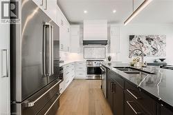 Gourmet kitchen with stainless steel appliances, dark stone countertops, light wood-finish flooring, white cabinetry, and a herringbone tile backsplash - 