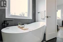Freestanding soaking tub with a matte black wall-mounted faucet, set against dark tile wainscoting - 