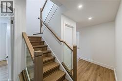 Wood-finish flooring, recessed lighting, white walls, and a staircase with wood treads, wood handrails, and glass panels - 
