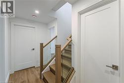 Wood-finish flooring, glass panel staircase with wood handrails, recessed lighting, white interior doors with contemporary hardware, and white wall finishes - 