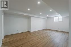 Spacious room featuring wood-finish flooring, white walls, recessed ceiling lighting, and a window with blinds - 