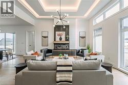 Spacious living area featuring a tray ceiling with integrated lighting, a striking linear chandelier, wood-finish flooring, and large windows - 