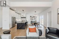 Open-concept living space with light wood-finish flooring, a modern kitchen featuring a waterfall island, stainless steel appliances, and white cabinetry - 