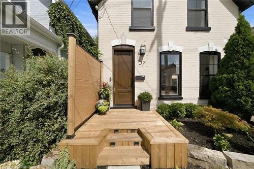 White brick exterior, wooden privacy screen, multi-level wooden deck, black framed windows, dark wood entry door - 57 Terrace Hill Street, Brantford, ON 