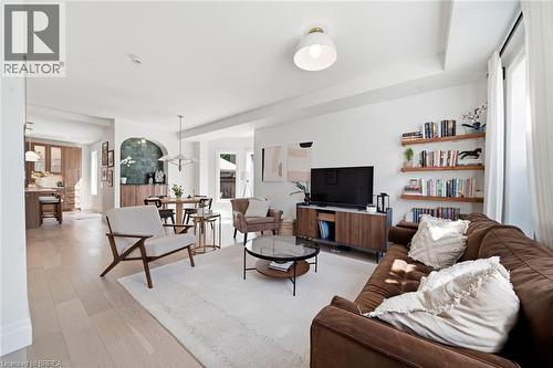 Light wood-finish flooring throughout, featuring a living area with built-in floating shelves, and an arched entry to the dining space - 57 Terrace Hill Street, Brantford, ON 
