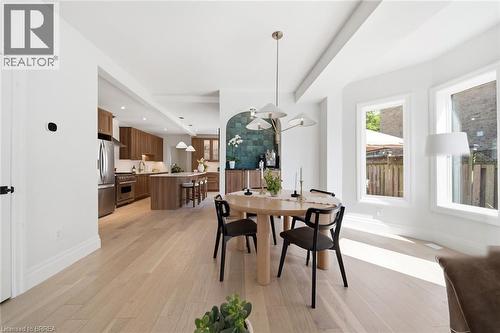 Open-concept dining area with light wood-finish flooring, a contemporary chandelier, and large windows - 57 Terrace Hill Street, Brantford, ON 