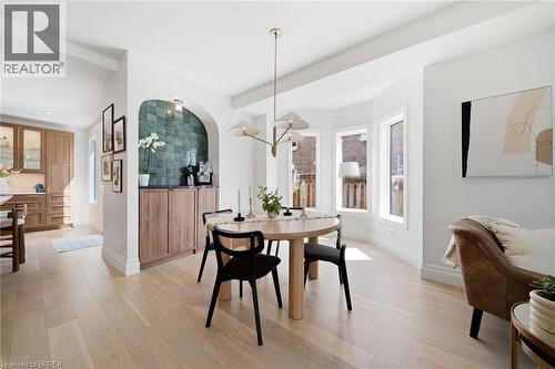 Light wood-finish flooring throughout, bay window with multiple panes, arched alcove with tiled accent wall, built-in cabinetry with wood-finish doors, and a contemporary chandelier - 57 Terrace Hill Street, Brantford, ON 