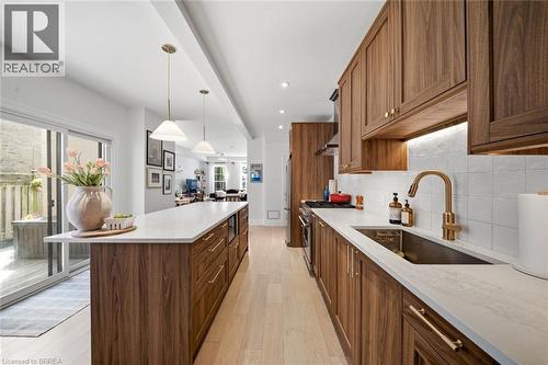 Kitchen featuring wood-finish cabinetry, light countertops, a stainless steel sink with a brass-finish faucet, and pendant lighting - 57 Terrace Hill Street, Brantford, ON 