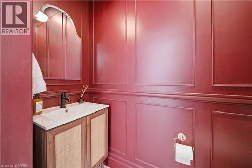 Wainscoting with decorative molding, vanity with rattan-front cabinetry, integrated sink, matte black faucet, and an arched wall mirror with an attached wall sconce - 57 Terrace Hill Street, Brantford, ON 