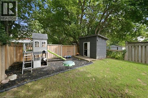 Spacious backyard with mature trees, a wooden privacy fence, a detached shed, and a dedicated play area with ground cover - 57 Terrace Hill Street, Brantford, ON 
