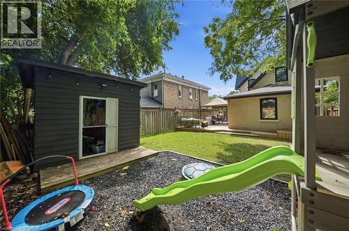 Expansive backyard featuring a manicured lawn, a gravel play area, a dark-paneled storage shed with a wood deck, and a raised wood patio with a gazebo - 57 Terrace Hill Street, Brantford, ON 