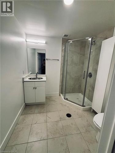 Corner glass-enclosed shower with tiled walls, white vanity with integrated sink, and square tile flooring - 1 Wellington Street Unit# 308, Brantford, ON 