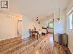 Wood-finish flooring throughout, recessed lighting, and a kitchen featuring white cabinetry, a stainless steel refrigerator, and a window with natural light - 