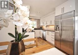 Kitchen featuring white high-gloss cabinetry, stainless steel appliances, dark countertops, and wood-finish flooring - 